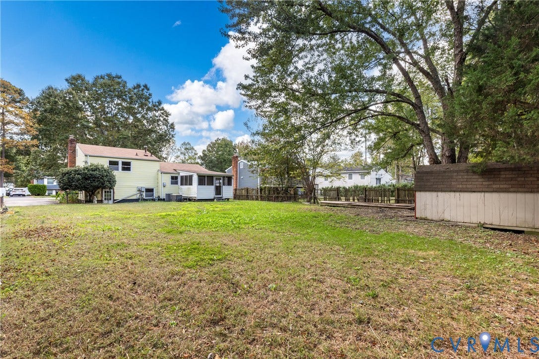 Expansive backyard featuring a level lawn, mature trees, a detached storage shed, and an enclosed porch