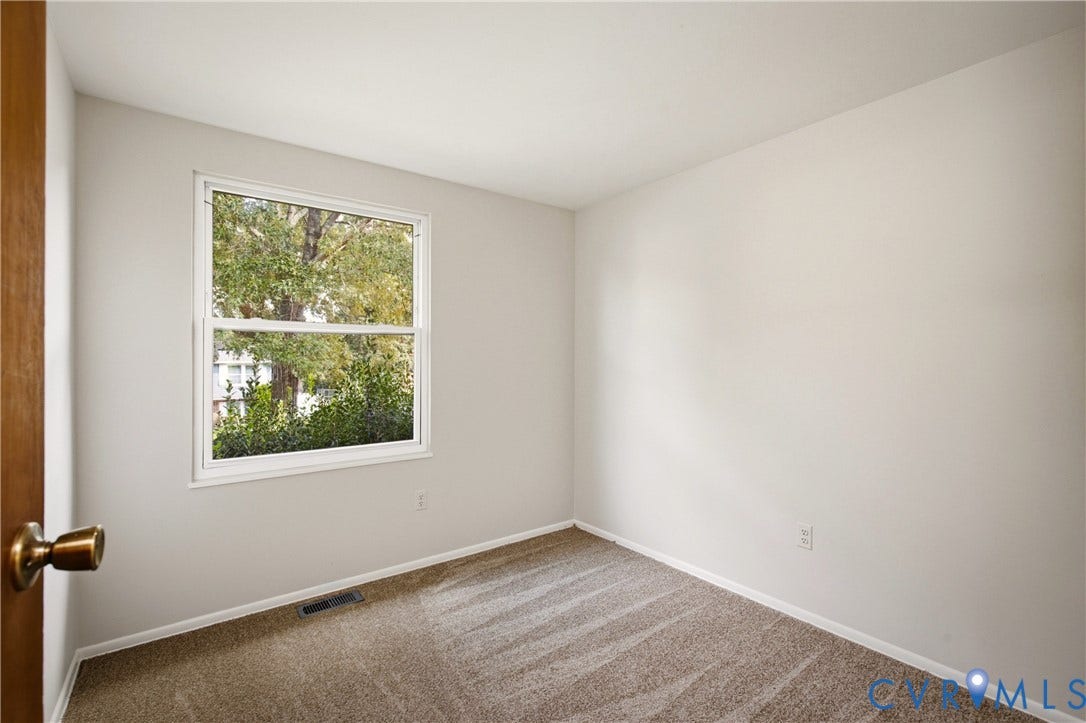 Neutral wall tones, plush wall-to-wall carpeting, and a double-hung window providing natural light