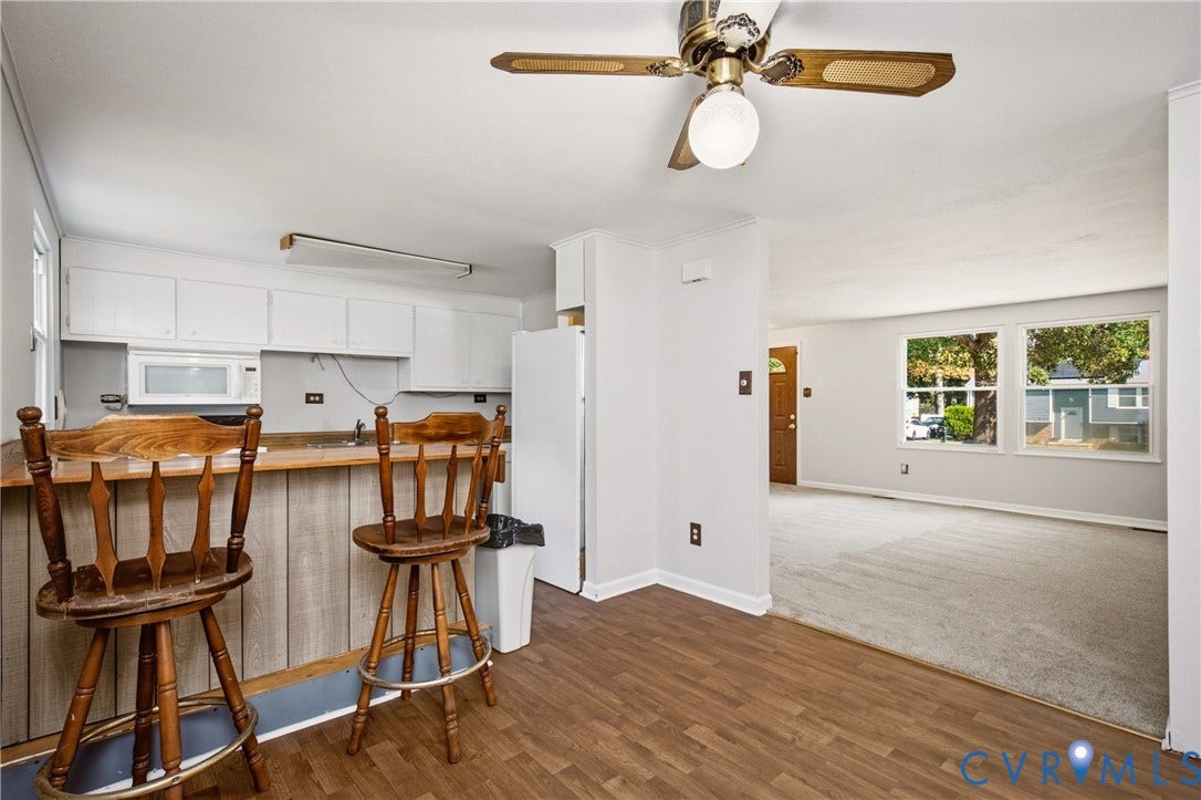 Kitchen featuring white cabinetry, a built-in microwave, wood-finish flooring, and a breakfast bar with wood paneling, complemented by a ceiling fan with integrated lighting