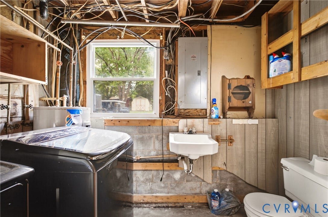 Utility area featuring a wall-mounted sink, exposed concrete block walls, wood-panel siding, and a double-hung window