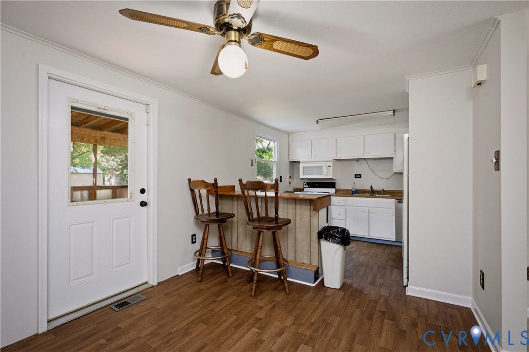 Kitchen featuring white cabinetry, wood-finish laminate counters, a built-in snack bar, and wood-finish flooring, complemented by a ceiling fan with integrated lighting and an exterior door with a window pane