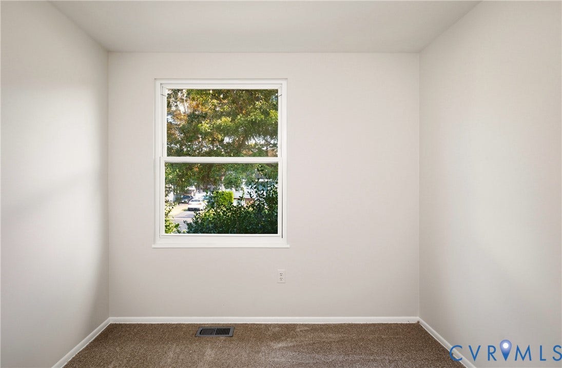 Neutral-toned interior walls featuring a double-hung window with exterior tree foliage