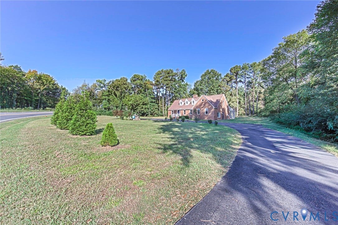 4124 Cogbill Road, Ampthill, VA 23234 Brick exterior residence featuring a gabled roofline with dormer windows, expansive lawn, paved driveway, and mature perimeter trees