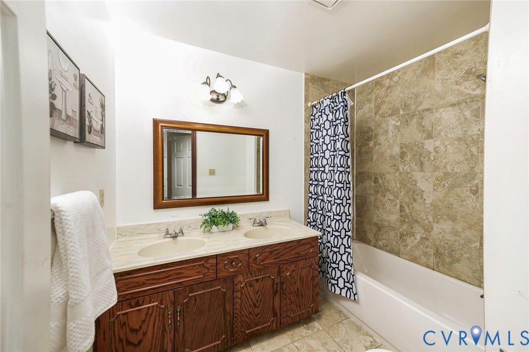4124 Cogbill Road, Ampthill, VA 23234 Bathroom featuring a dual-sink vanity with solid-surface countertops, wood-finish cabinetry, a framed wall mirror, and a tile-surround bathtub