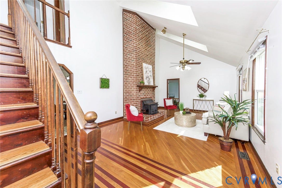 4124 Cogbill Road, Ampthill, VA 23234 Living area featuring a floor-to-ceiling brick fireplace, wood-finish flooring with inlay detailing, vaulted ceiling with skylights, and an open staircase with a wooden balustrade