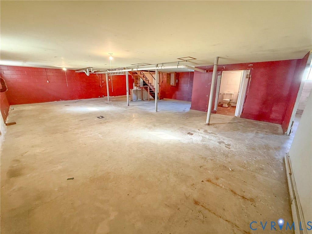 109 Rock Castle Avenue, Crewe, VA 23930 Open-concept interior space featuring painted masonry walls, concrete flooring, exposed ceiling structural elements, support columns, and an enclosed room with a toilet