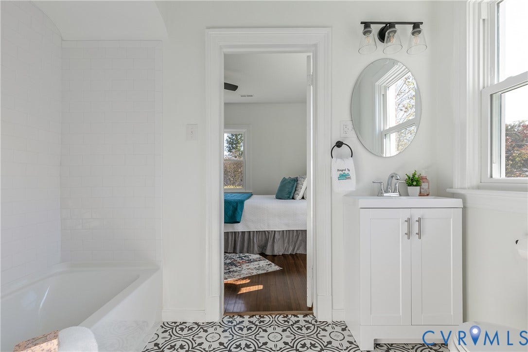 24 N Elm Avenue, Henrico, VA 23075 Bathroom featuring a white vanity cabinet with a stone-top sink, oval wall-mounted mirror, three-light fixture, tub-shower combination with white subway tile surround, and decorative patterned floor tile