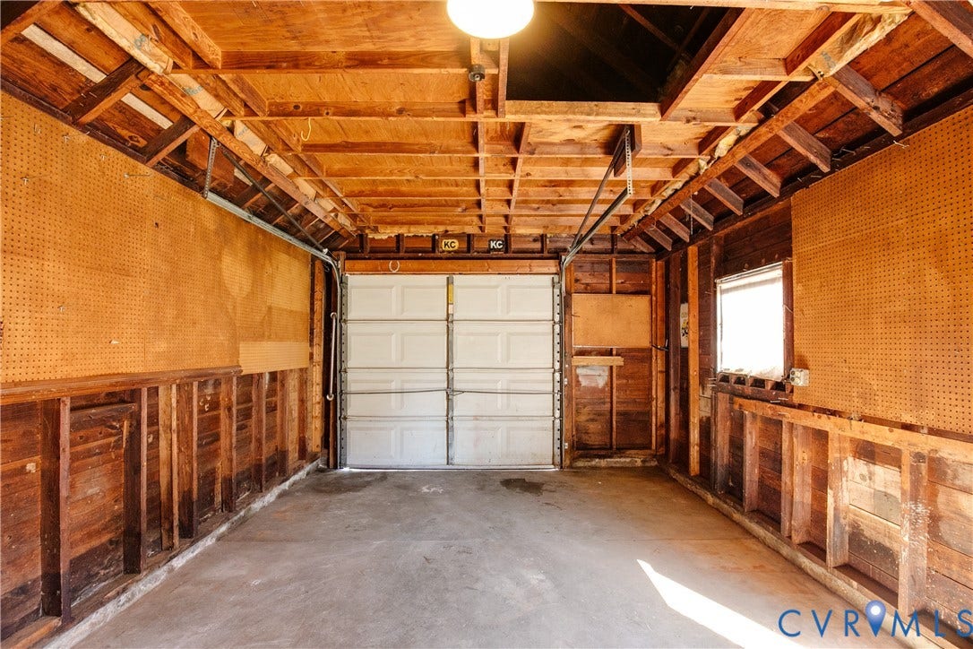 24 N Elm Avenue, Henrico, VA 23075 Detached garage featuring exposed wood-stud framing, pegboard wall panels, a concrete floor, an overhead sectional garage door, and a single window