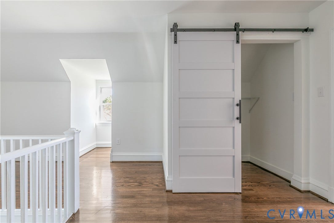 24 N Elm Avenue, Henrico, VA 23075 White five-panel sliding barn door with matte black hardware, wood-finish flooring, and white railing featuring a vertical baluster design