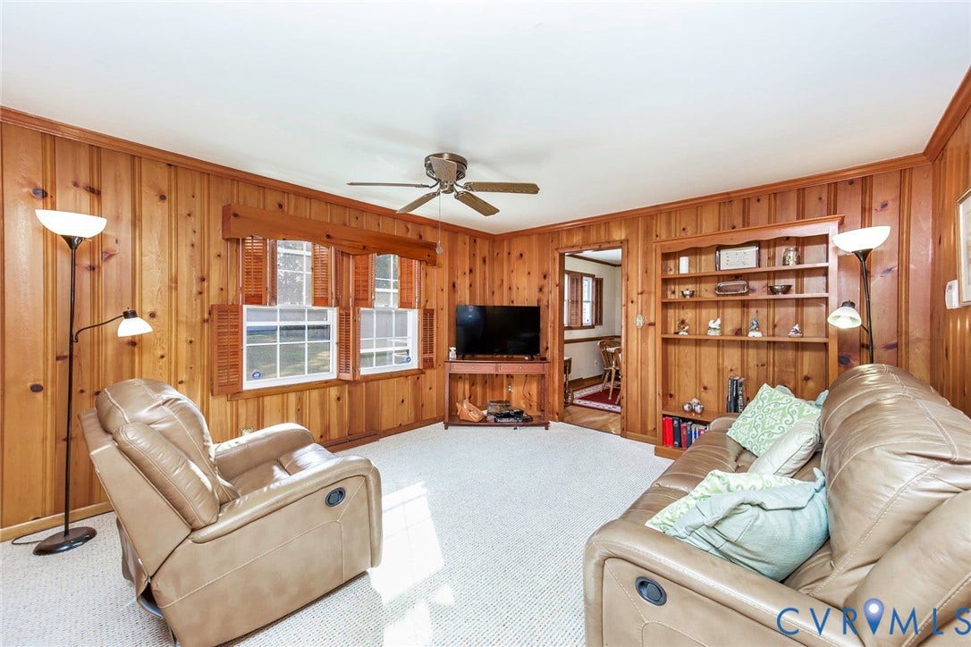 700 Lakeside Drive, Emporia, Emporia, VA 23847 Living area featuring vertical wood-paneled walls, built-in floor-to-ceiling shelving, carpeted flooring, and a central ceiling fan