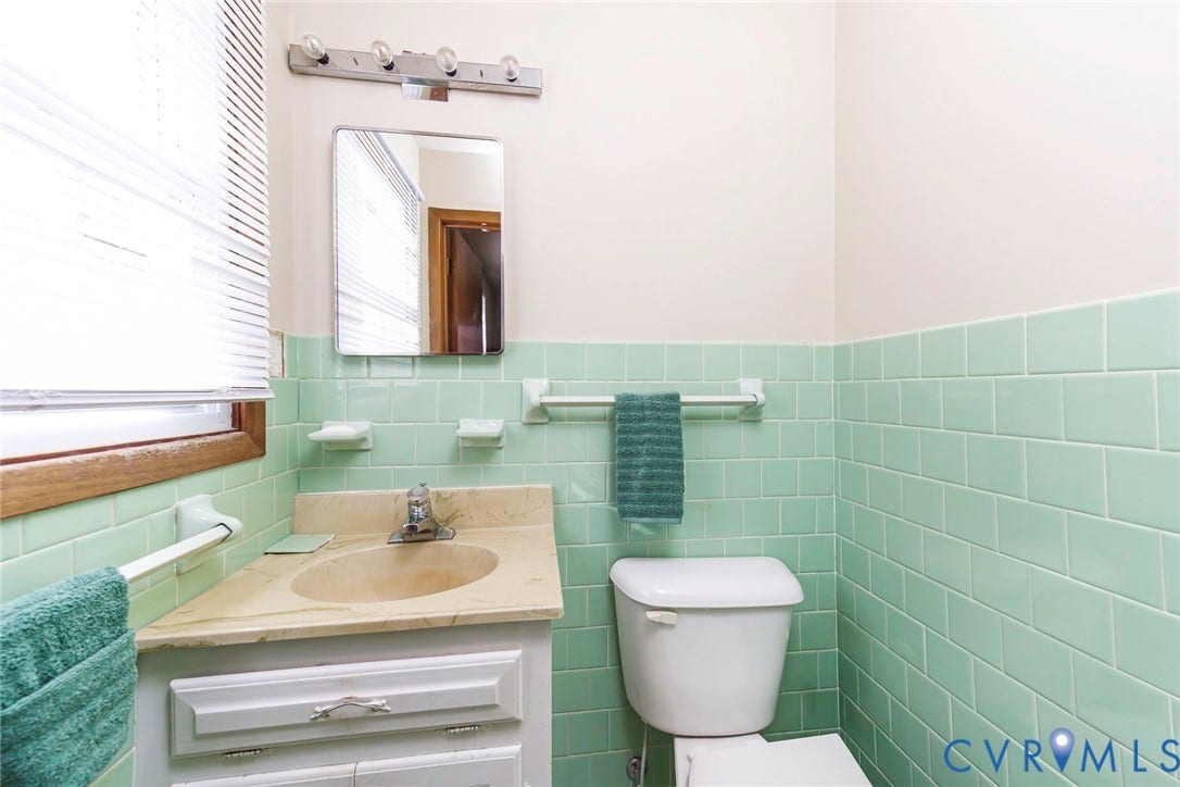 700 Lakeside Drive, Emporia, Emporia, VA 23847 Bathroom featuring light green ceramic wall tile, a stone-finish vanity countertop with an integrated oval sink, a wall-mounted vanity mirror, and an overhead four-bulb light fixture