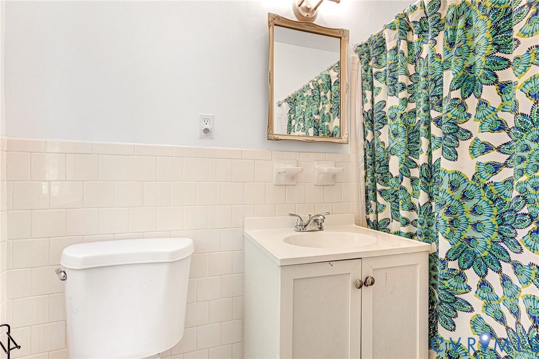 1526 Westshire Lane, Henrico, VA 23238 Bathroom featuring white subway tile wall wainscoting, a white vanity cabinet with an integrated countertop sink, a dual-handle faucet, and an attached wall-mounted mirror