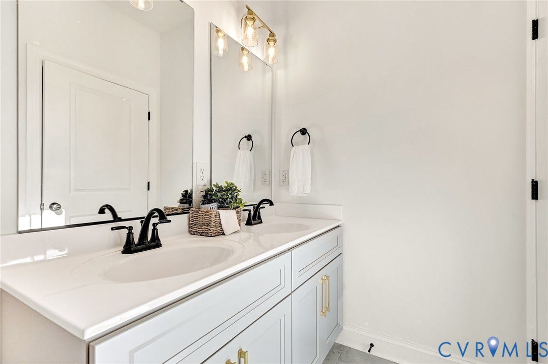 1807.5 Gordon Avenue, Oak Grove, Oak Grove, VA 23224 Double vanity featuring shaker-style cabinetry, white countertop with dual integrated sinks, matte black widespread faucets, and large-format wall mirrors with gold-tone overhead lighting