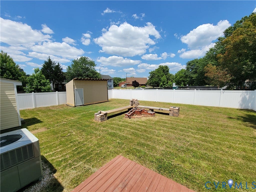 Backyard featuring a wood deck, built-in brick fire pit with stone-base benches, a detached storage shed, and a privacy fence
