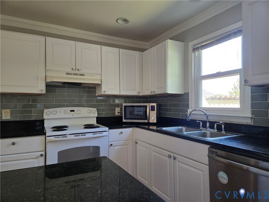 Kitchen featuring white shaker-style cabinetry, dark stone countertops, gray subway tile backsplash, stainless steel double-basin sink, and built-in appliances