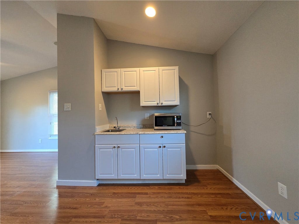 Wet bar featuring white cabinetry, stone-finish countertops, stainless steel sink, and wood-finish flooring