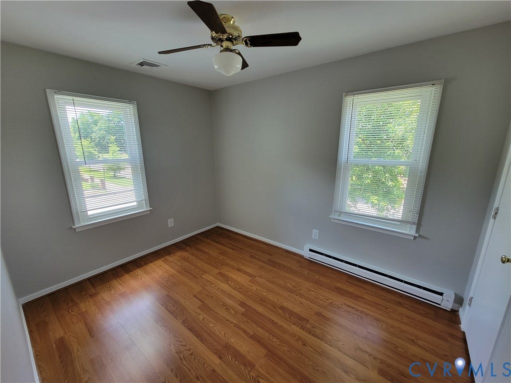 Room featuring wood-finish flooring, dual windows, and a central ceiling fan with integrated light fixture