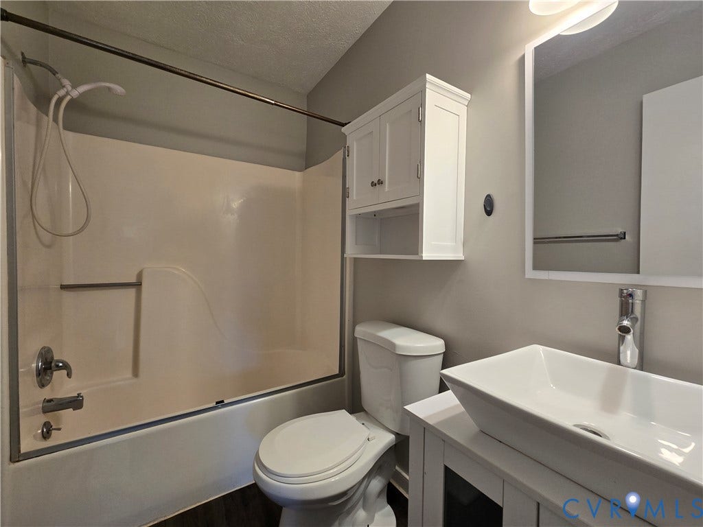 Bathroom featuring a rectangular vessel sink with a chrome faucet, white vanity cabinet, wall-mounted storage cabinetry, and a shower-tub combination with a handheld shower head