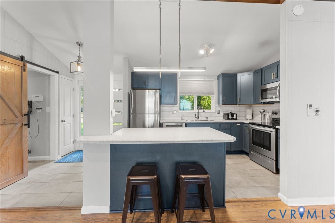 Kitchen featuring blue cabinetry, stone-finish countertops, stainless steel appliances, a subway tile backsplash, and a sliding wood-finish barn door