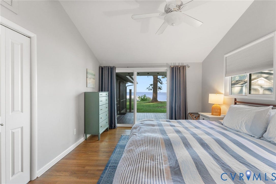 Vaulted ceiling with integrated paddle fan, wood-finish flooring, sliding glass door, and natural water backdrop