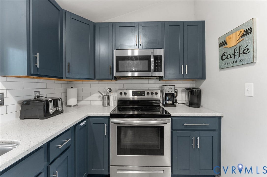 Kitchen featuring blue shaker-style cabinetry, white solid-surface countertops, a white subway tile backsplash, and stainless steel appliances including a built-in microwave and range