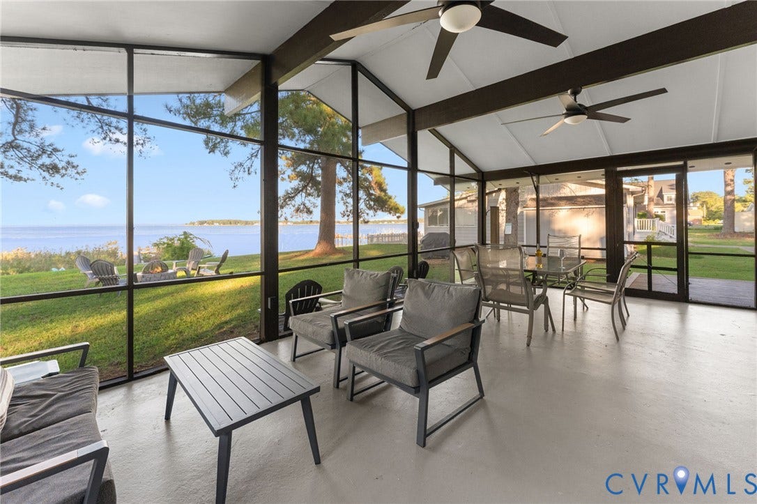 Screened-in porch featuring exposed dark wood beams, dual ceiling fans, and floor-to-ceiling metal-framed screens overlooking the water