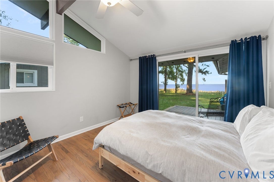 Vaulted ceilings, wood-finish flooring, clerestory windows, and sliding glass doors opening to an exterior patio with water frontage