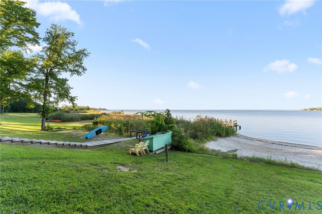 Waterfront property featuring a private wooden pier, natural sandy shoreline, expansive grass lawn, and mature trees