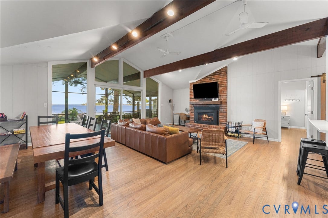 Vaulted ceiling featuring exposed timber beams, floor-to-ceiling windows, wood-finish flooring, and a brick-surround fireplace with a timber mantel