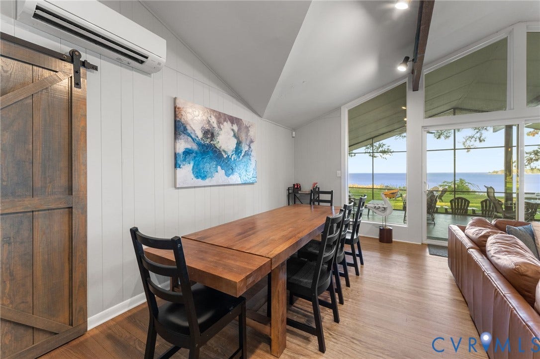 Vaulted ceilings with exposed timber beams, expansive floor-to-ceiling windows, wood-finish flooring, and a sliding barn door