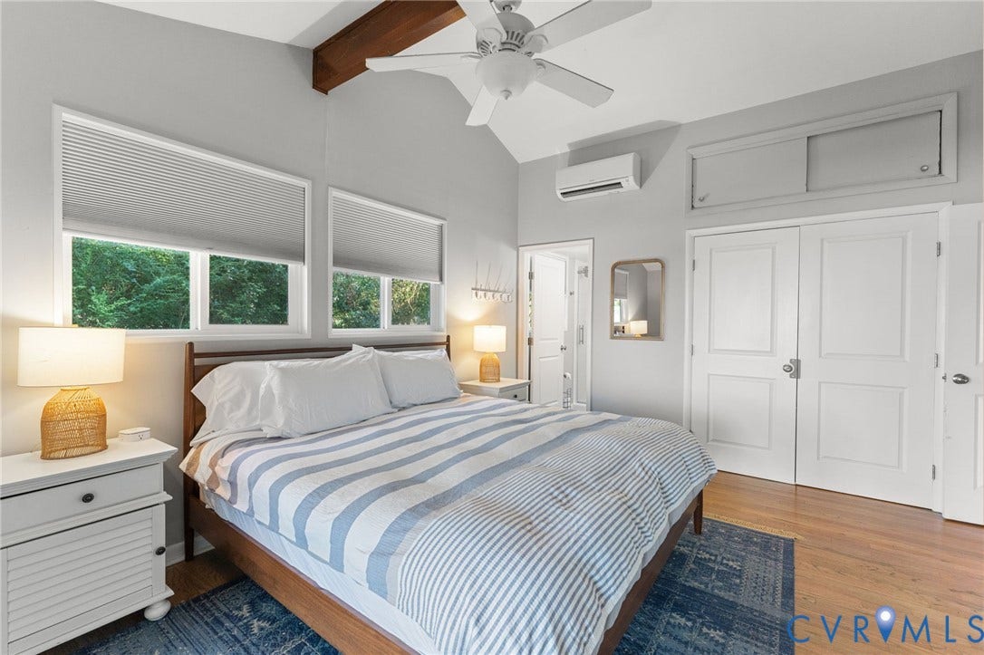 Vaulted ceiling featuring an exposed wood beam, wood-finish flooring, dual-pane windows with integrated blinds, wall-mounted ductless climate control system, and a multi-panel door entry