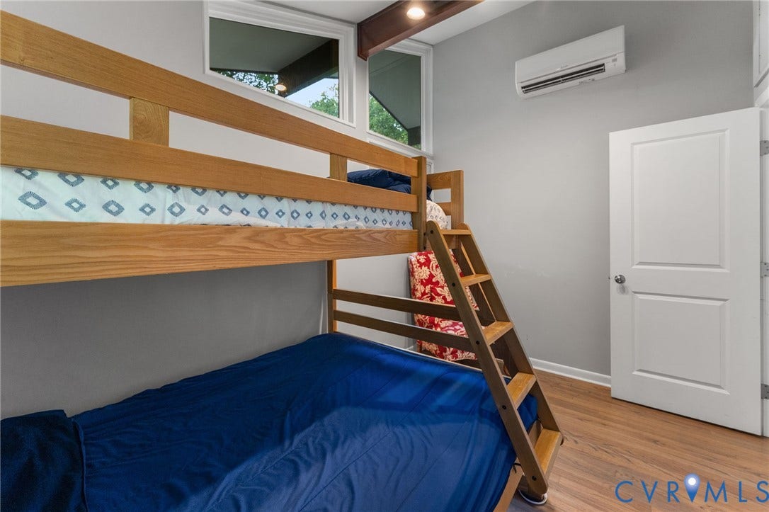 Room with wood-finish flooring, clerestory windows, exposed ceiling beam, and wall-mounted ductless heating and cooling unit
