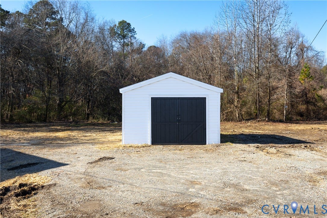 6280 Monahan Road, Henrico, VA 23231 Detached outbuilding featuring a white exterior, gable roofline, and dual-swing dark-toned doors, positioned on a gravel lot