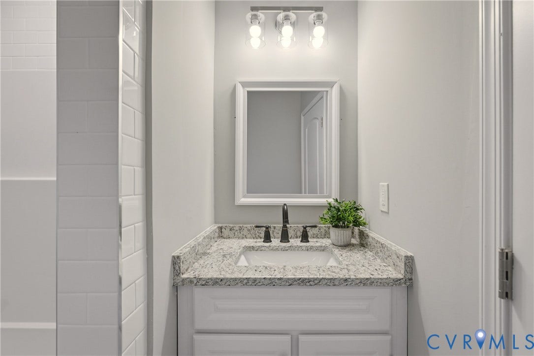 6280 Monahan Road, Henrico, VA 23231 Bathroom vanity featuring a stone-composite countertop, undermount sink, three-light fixture, framed mirror, and white shaker-style cabinetry