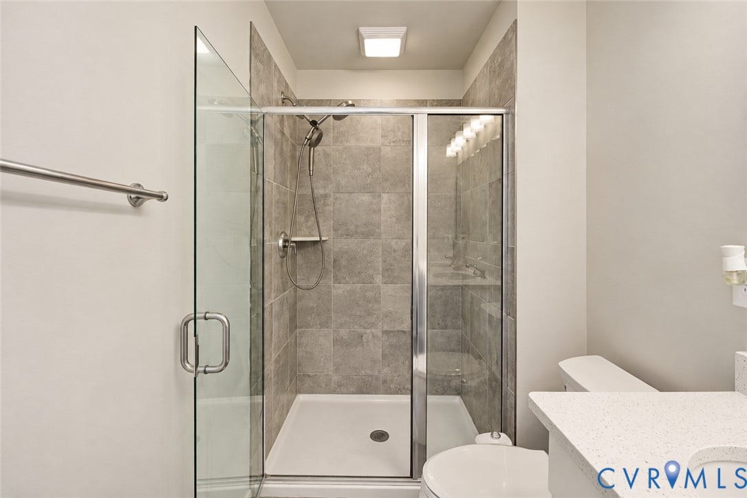 500 Rivanna Hill Way, Glen Allen, VA 23060 Walk-in shower featuring a glass enclosure, oversized neutral tile surround, and adjustable handheld showerhead, complemented by a stone-composite countertop with a recessed sink