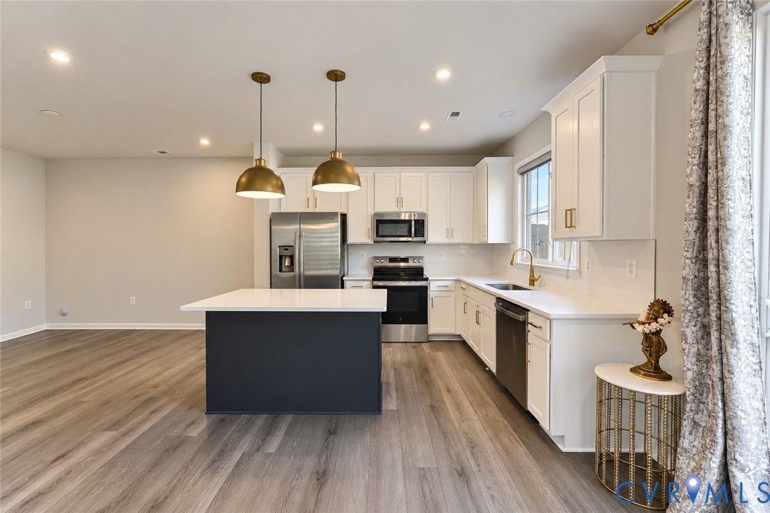 500 Rivanna Hill Way, Glen Allen, VA 23060 Kitchen featuring white cabinetry, wood-finish flooring, a central island with a solid-surface countertop, stainless steel appliances, and brass-tone pendant lighting