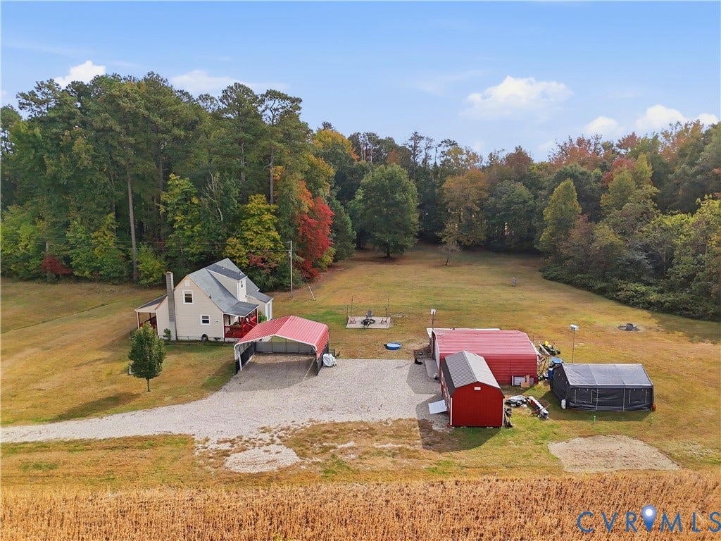 16401 Anderson Drive, Disputanta, VA 23833 Expansive lot featuring mature perimeter trees, a detached multi-bay metal structure, a gravel driveway, and a residential building with a covered exterior entry