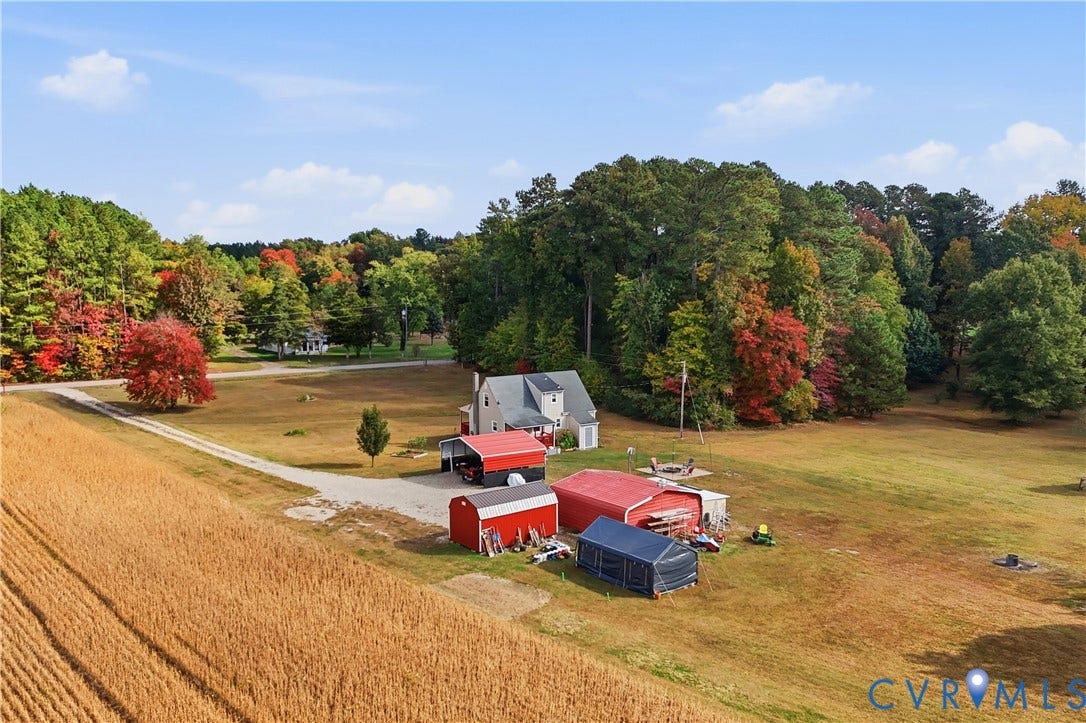 16401 Anderson Drive, Disputanta, VA 23833 Extensive acreage featuring multiple outbuildings, metal-roofed storage structures, a gravel driveway, and mature perimeter trees