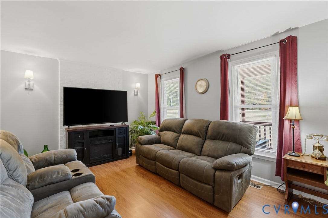 16401 Anderson Drive, Disputanta, VA 23833 Living area featuring wood-finish flooring, white painted brick accent wall, and dual wall-mounted light fixtures
