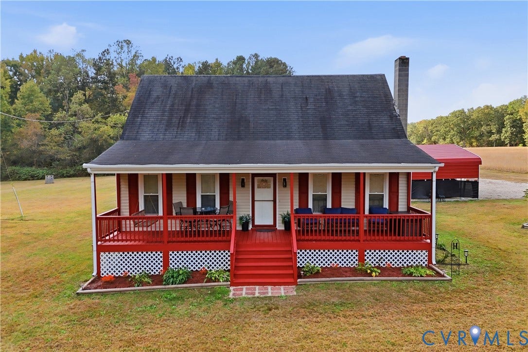 16401 Anderson Drive, Disputanta, VA 23833 Single-story residence featuring a full-width covered front porch, red wood railings, decorative lattice skirting, exterior masonry chimney, and metal-roofed detached structure
