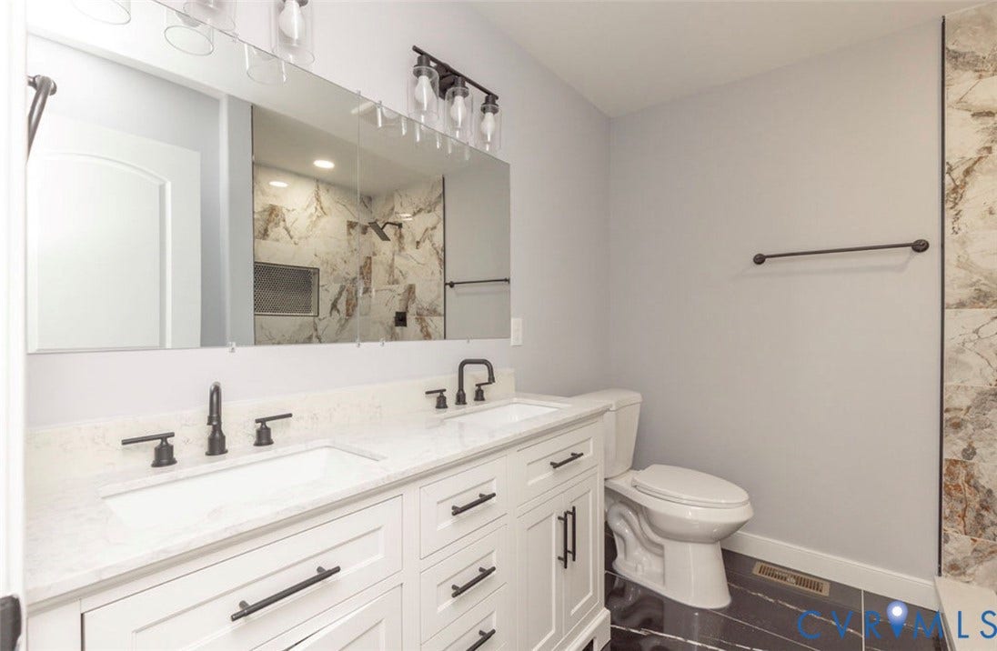 25604 Greensville Avenue, West Petersburg, Dinwiddie, VA 23803 Double vanity with white cabinetry, quartz-surface countertops, rectangular undermount sinks, matte black hardware, and an oversized vanity mirror with overhead glass-shade lighting