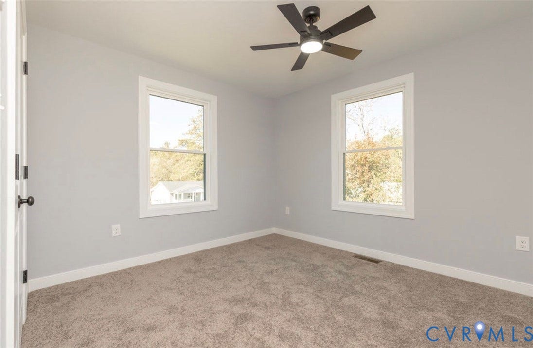 25604 Greensville Avenue, West Petersburg, Dinwiddie, VA 23803 Neutral-toned interior featuring wall-to-wall carpeting, dual double-hung windows, and a matte black ceiling fan with integrated lighting