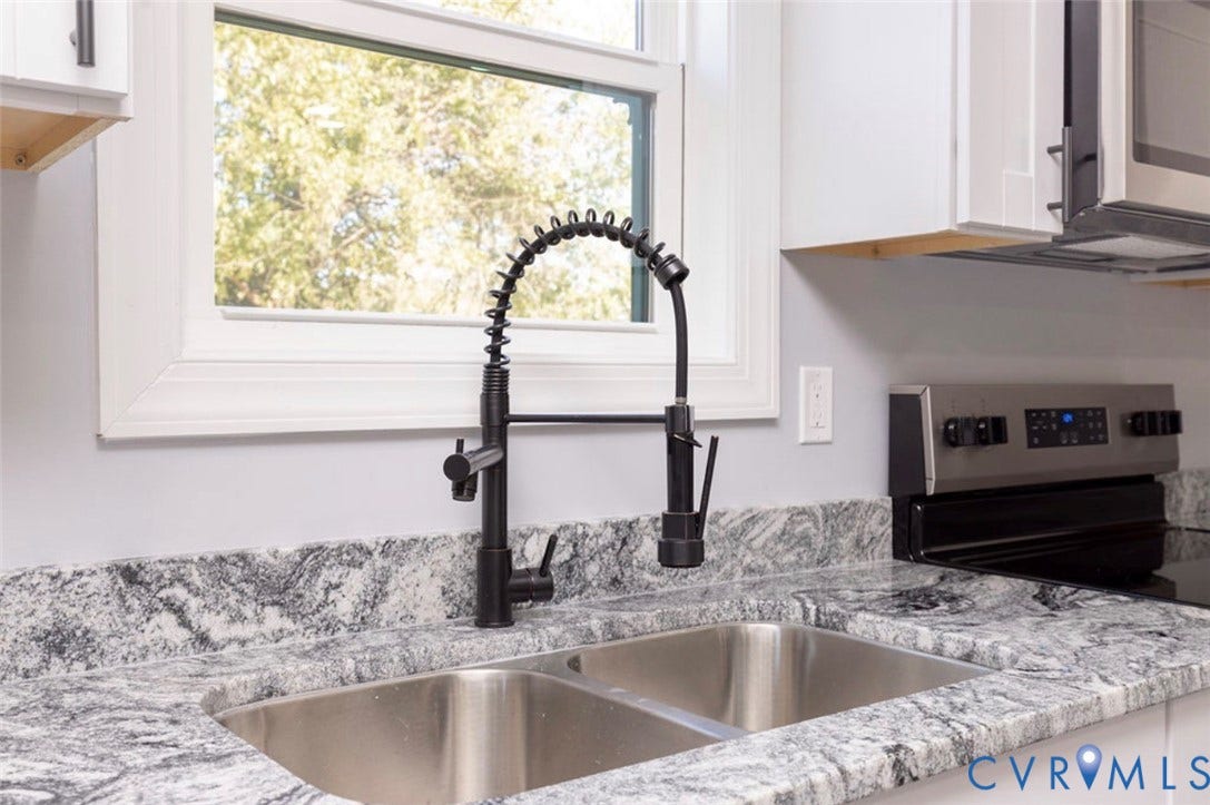 25604 Greensville Avenue, West Petersburg, Dinwiddie, VA 23803 Dual-basin stainless steel sink featuring a matte black industrial-style pull-down faucet, stone-surfaced countertops with integrated backsplash, and crisp white cabinetry