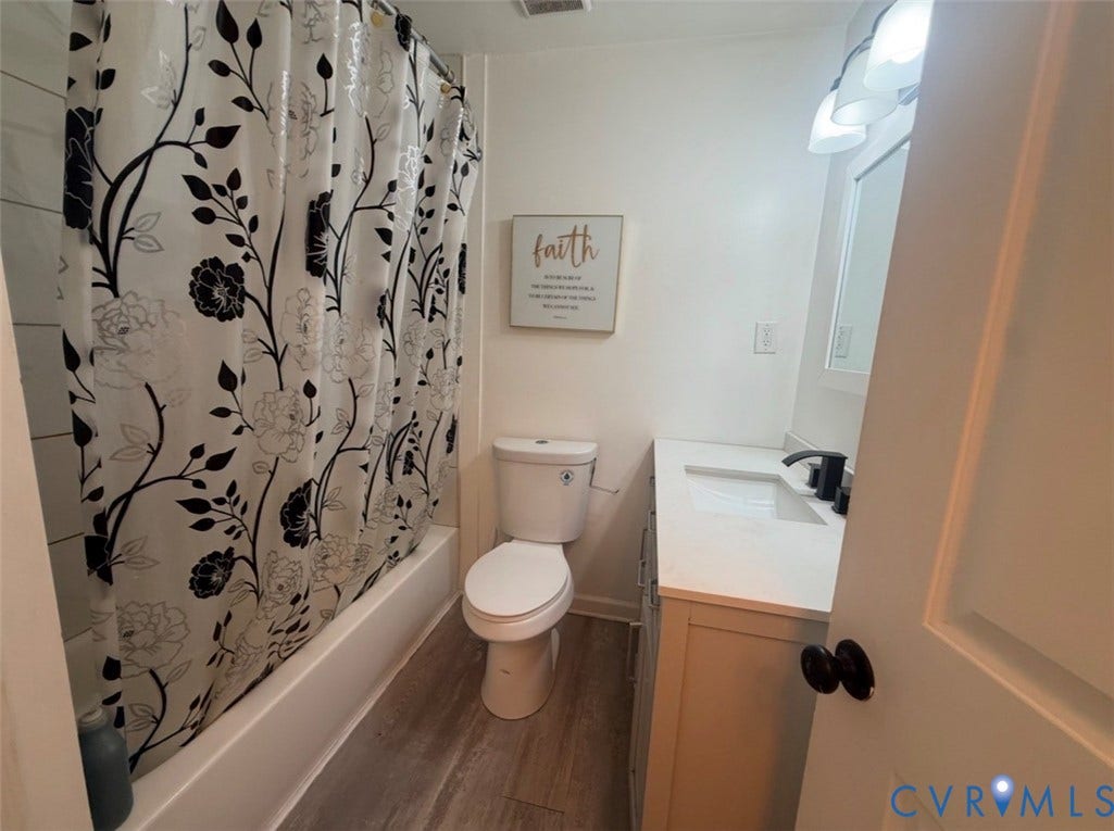 Bathroom featuring a vanity with a white countertop and rectangular integrated sink, matte black faucet, wood-finish flooring, and a shower-tub combination