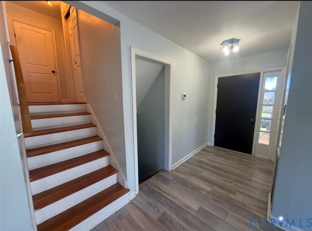 Entryway featuring wood-finish flooring, a solid-paneled door with an integrated sidelight, and a staircase with wood treads and white risers