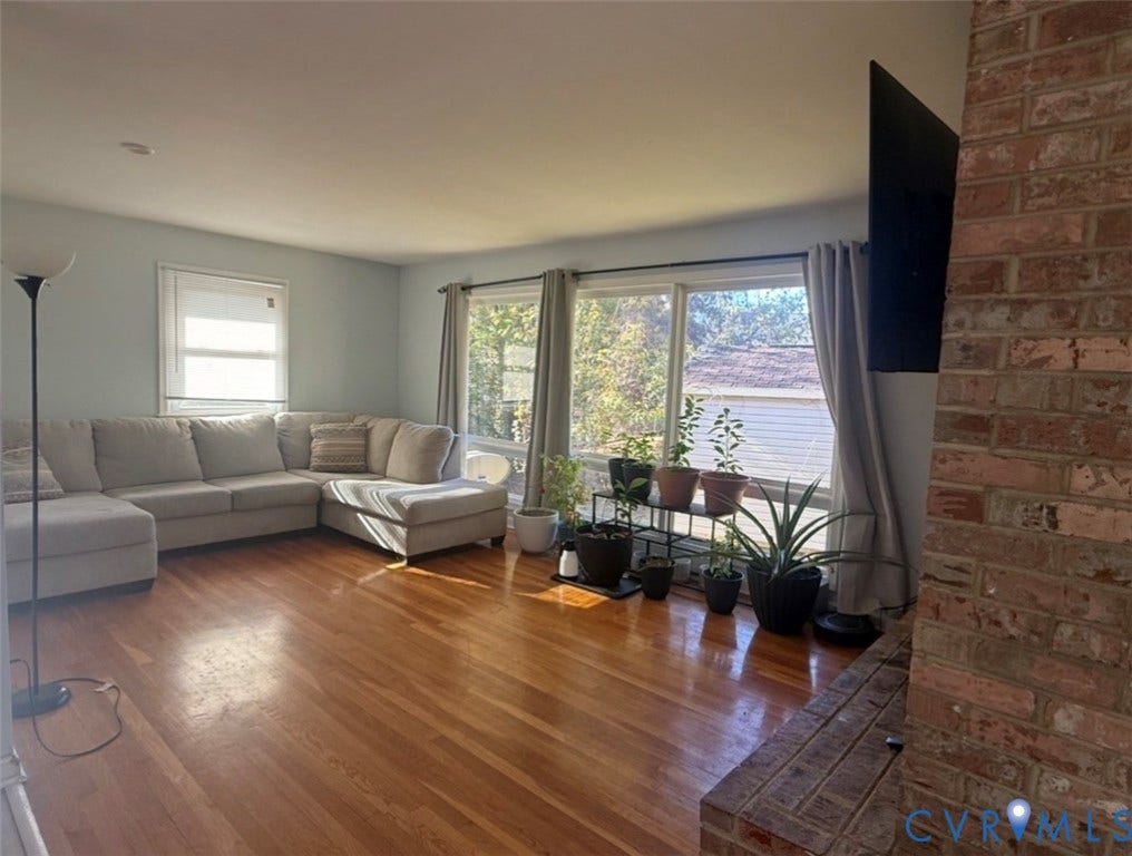 Wood-finish flooring, floor-to-ceiling multi-panel windows, and exposed red brick chimney feature