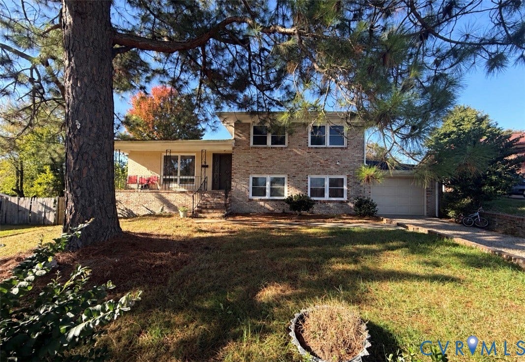 Split-level exterior featuring a brick facade, integrated garage, front porch with wrought-iron railing, and mature landscaping