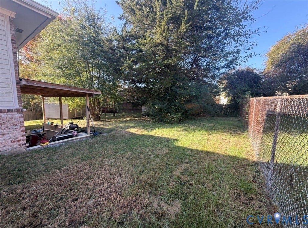 Backyard featuring a covered patio, grass lawn, mature trees, and chain-link perimeter fencing