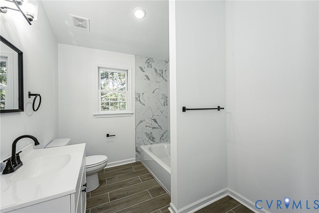 10100 Brittonwood Drive, Chesterfield, VA 23237 Bathroom featuring wood-finish flooring, a white vanity with a solid-surface countertop, matte black fixtures, and a tub surround with large-format decorative tile