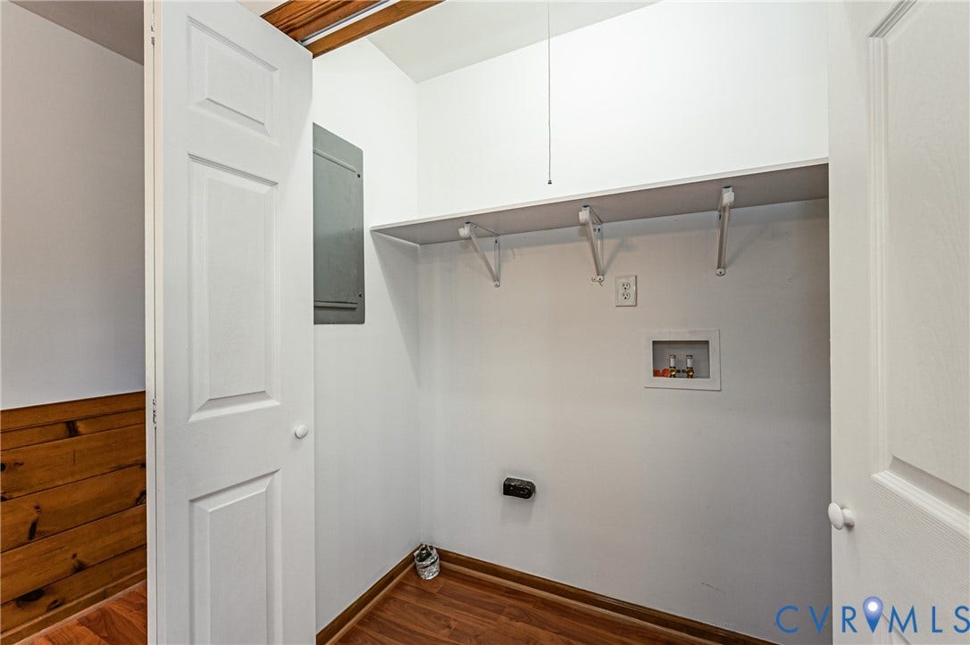 10100 Brittonwood Drive, Chesterfield, VA 23237 Utility closet featuring wood-finish flooring, a white overhead storage shelf with bracket supports, a recessed plumbing hookup box, and an electrical service panel